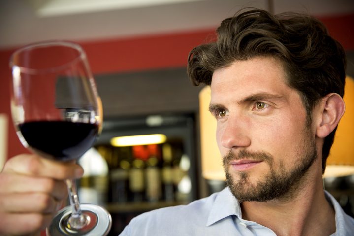 Mann begutachtet ein Glas Rotwein