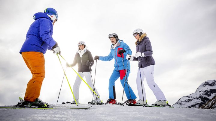 Drei Erwachsene stehen auf Skiern und ihr Skilehrer erklärt Ihnen Techniken