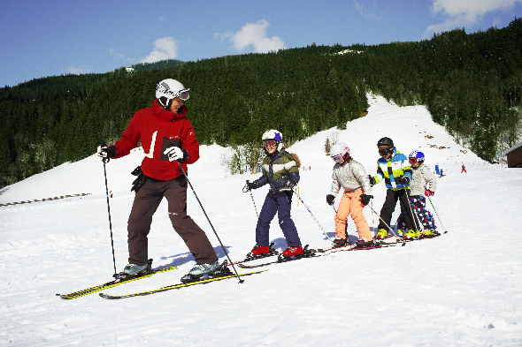 Skilehrer fährt auf Skiern und seine Schüler fahren ihm hinterher