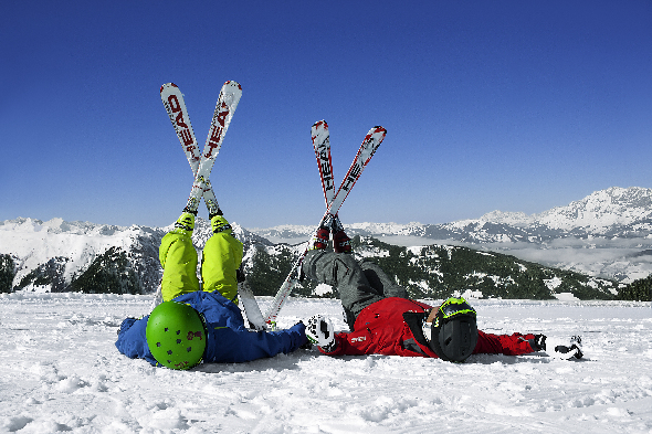 Zwei Personen liegen in Skikleidung im Schnee und halten ihre Füße, mit den Skiern daran, in die Luft