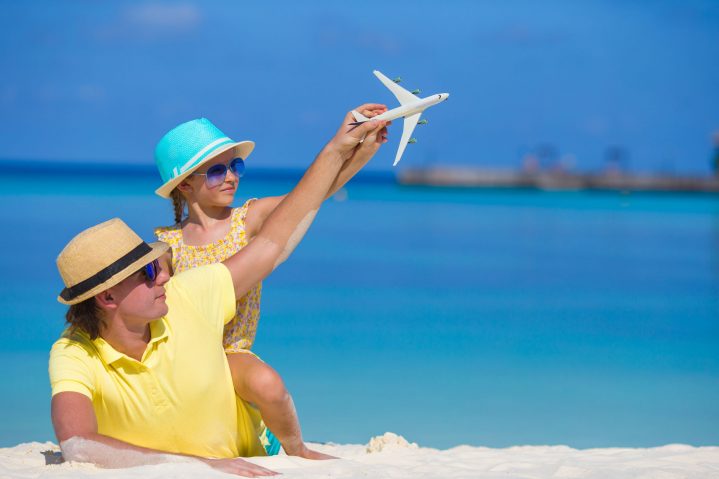Vater und Tochter am Strand mit Spielzeugflugzeug nachhaltiger Urlaub