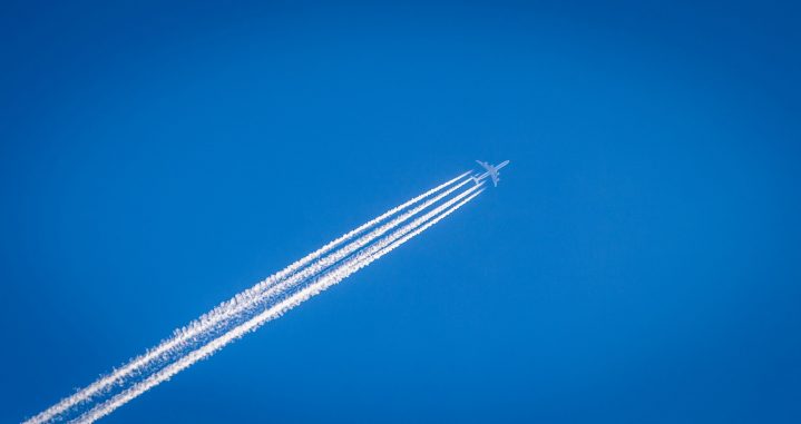 Flugzeug mit Kondenzstreifen am wolkenlosen Himmel Photo by William Hook on Unsplash