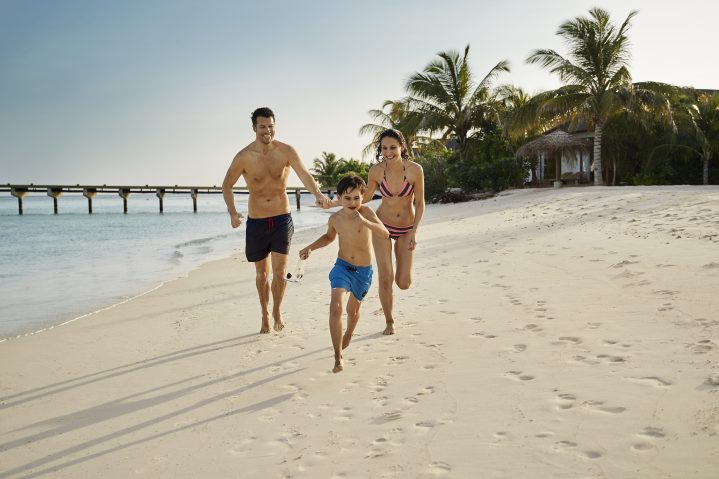 Eltern mit Kind laufen den Strand entlang