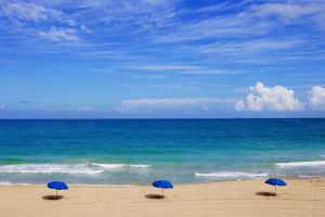 Ein einsamer Strand mit blauen Sonnenschirmen.